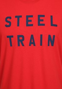 Fondo de tela roja con letras mayúsculas en negrita de color azul oscuro que dicen "STEEL TRAIN" en dos filas escalonadas.