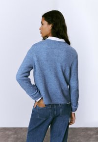 Suéter azul de punto con un corte relajado, escote redondo y puños acanalados, combinado con unos vaqueros de talle alto.