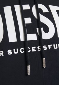 Svart sweatshirt med stor vit text "DIESEL FÖR FRAMGÅNG" och svarta dragsnören med metallspetsar. Mjuk tyg med en slät textur.