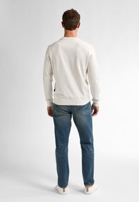 White speckled sweatshirt with a rounded neck and long sleeves, paired with blue denim jeans and cream-colored shoes.