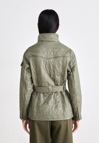 Gequilte olijfgroene jas met een hoge kraag, een taille met riem en ritsmanchetten. Het heeft een ruitpatroon en een gestructureerd ontwerp.