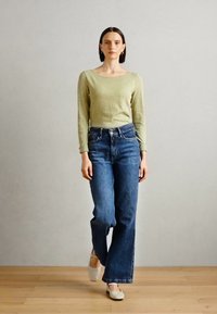 Lysegrønn langermet topp, løse blå jeans og hvite sko. Jeansene har høy midje, mens toppen har en avrundet utrigning.