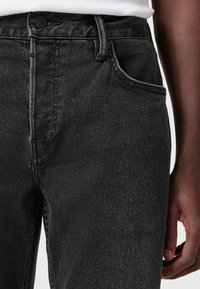 Musta farkkuhousut, joissa on klassinen leikkaus ja hienovaraiset ompeleet sekä viisi taskua. Materiaali on teksturoitua ja hieman haalistunutta.