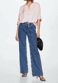 Blusa rosa chiaro con scollo a V e cordoncino, abbinata a jeans blu a vita alta e gamba larga e borsa nera. Tessuto morbido e look informale.