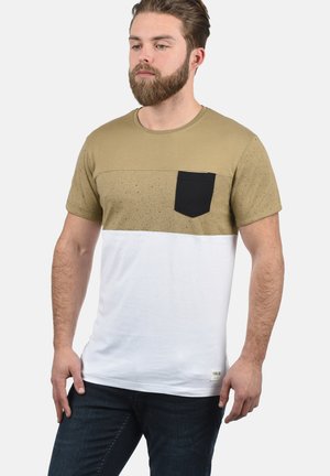 Majica kratkih rukava s gornjim dijelom u kaki boji koji ima točkasti uzorak, crnom džepom na prsima i donjim dijelom u bijeloj boji.