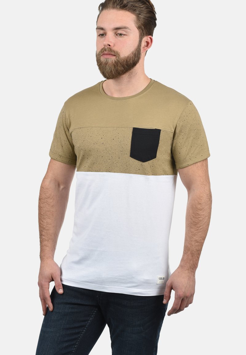 T-shirt med korte ærmer med en khaki topsektion med spraglet tekstur, en sort brystlomme og en hvid nederste sektion.