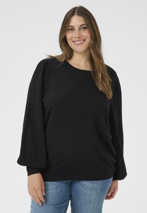 Black pullover sweater with textured balloon sleeves. Soft fabric, round neckline, and ribbed cuffs and hem. Worn with blue jeans.
