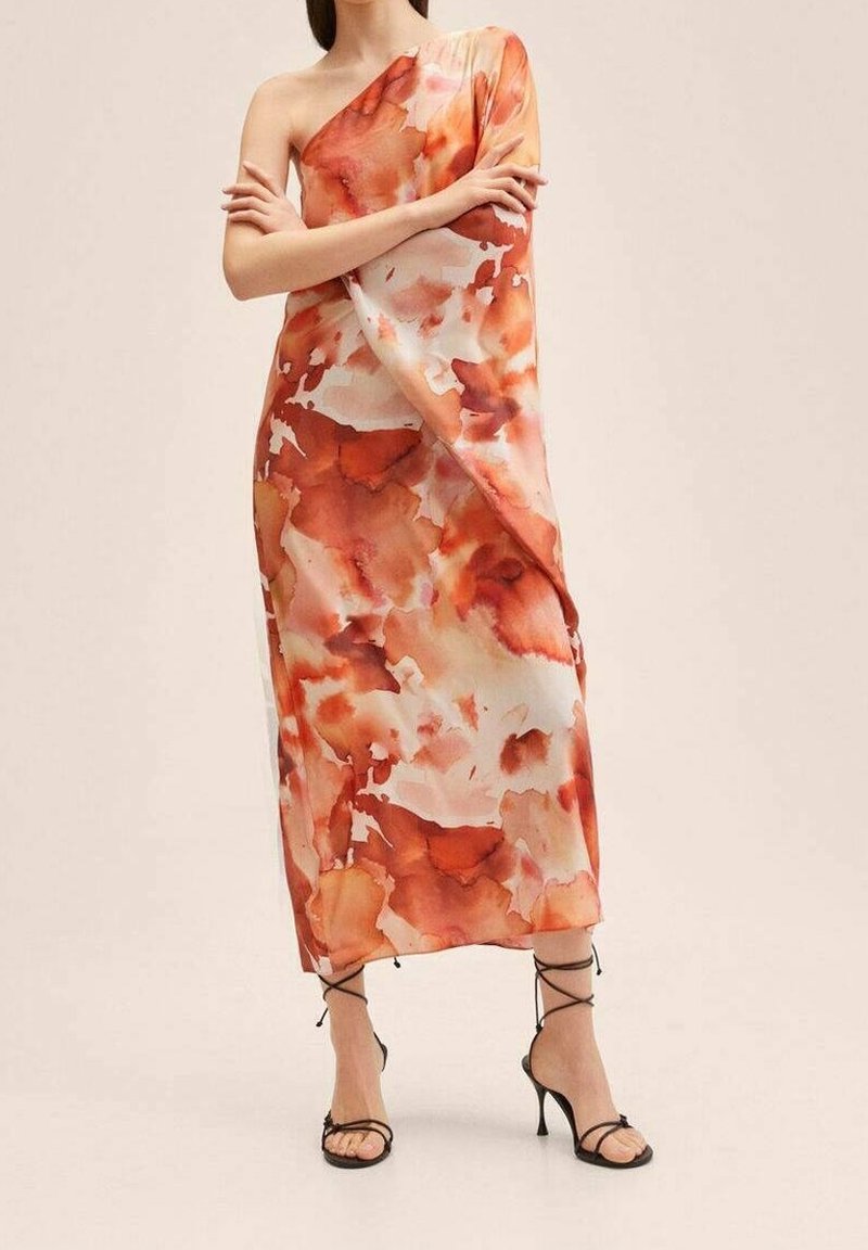 Femme portant une robe asymétrique longue jusqu'aux chevilles avec des motifs aquarelle orange et blancs, associée à des sandales à talons hauts noires à lanières.