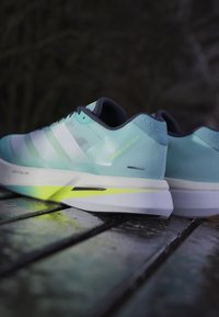 Light blue running shoes with white stripes, textured upper, neon accents, and a chunky white sole. Features branding on the side.