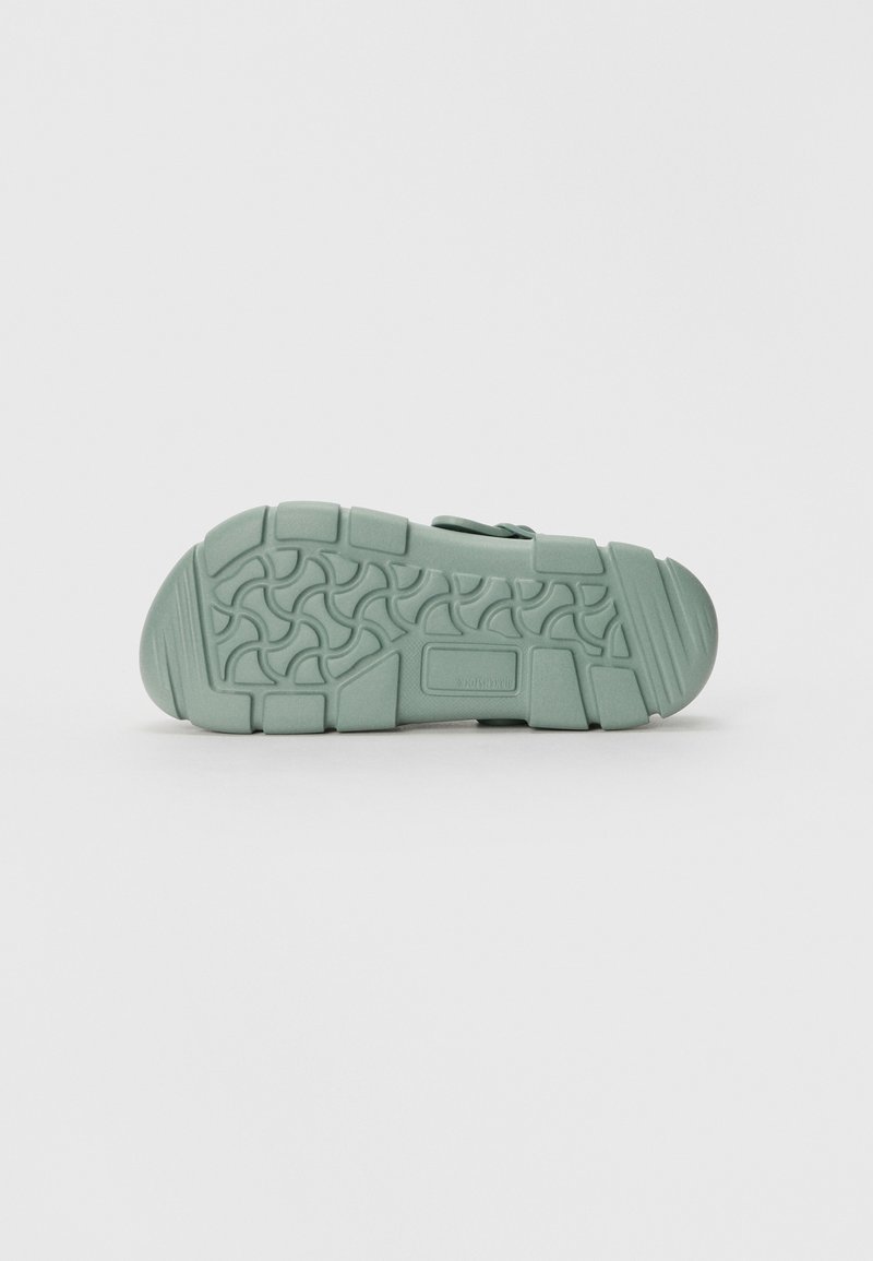 Suola di scarpa verde chiaro in gomma testurizzata per una buona aderenza, con un motivo ondulato e tacco piatto, progettata per comfort e stabilità.