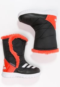 Czarne ocieplane buty z białą podeszwą, z pomarańczowym sztucznym futrem na krawędzi, trzema białymi paskami po boku oraz wytrzymałą górną konstrukcją.