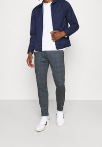 Navy blue lightweight jacket, white t-shirt, gray plaid trousers, and white sneakers with black accents. Focus on casual, modern style.