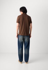 Braunes Polohemd aus Baumwolle, kombiniert mit lässigen, leicht sitzenden hellblauen Jeans mit einem ausgewaschenen Muster. Sichtbares, lässiges Schuhwerk.