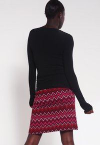 Top nero a maniche lunghe abbinato a una gonna a zigzag nei toni del rosso e del rosa, con una silhouette aderente e una texture morbida.