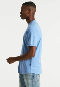 T-shirt azzurro chiaro a maniche corte con scollatura rotonda, vestibilità comoda, texture sottile e polsini arrotolati, abbinato a jeans azzurri chiari.