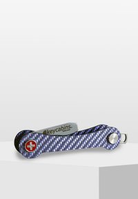 Multiverktyg i form av en nyckelhållare med kolfiberstruktur, lila färg, silverdetaljer och ett rött korsemblem. Har en solid och stilren design.