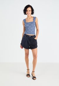Top scurt cu model albastru și decolteu pătrat, asortat cu pantaloni scurți din denim închis, cu talie înaltă, și sandale negre cu curele.