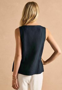 Särik, millel puuduvad varrukad, on valmistatud tekstureeritud kangast, sellel on sirge lõige ja peened küljeavad, ning see on kombineeritud heledate pükstega.