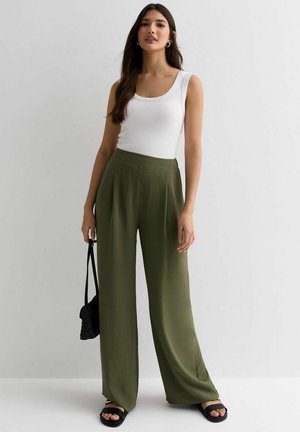 Top blanco sin mangas, pantalones verdes de pierna ancha y sandalias negras. Los pantalones tienen una textura fluida; el conjunto incluye un pequeño bolso negro.