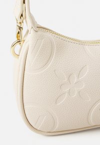 Bolso de piel color crema con acabado texturizado, diseño floral en relieve y herrajes dorados. Presenta un cierre de cremallera y forma curva.