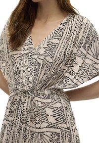 Musta ja beige kuvioitu mekko, jossa on V-pääntie, löysät hihat ja joustava vyötärönauha; valmistettu tekstuuri- ja kevyestä kankaasta.