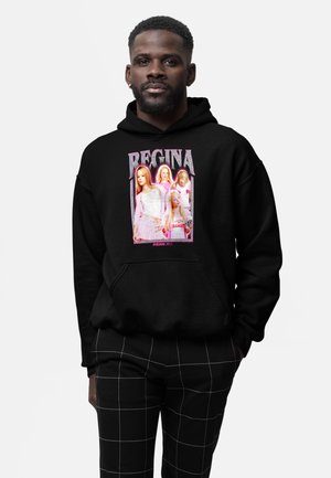 Mand iført sort hættetrøje med "Regina" og fire piger i pink outfits fra "Mean Girls" trykt på fronten, kombineret med sorte bukser med hvidt tern.