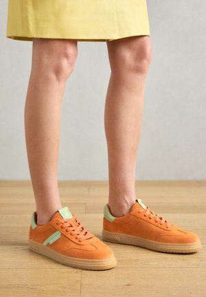 Baskets en daim orange avec une accentuation vert menthe, présentant un design classique bas, un bout rond et une semelle en caoutchouc gomme. Détail de surface texturé.
