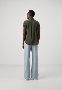 Olivengrønn kortermet bluse med ryggfold, parret med lyseblå vide bukser. Glatt stoff med en avslappet passform.