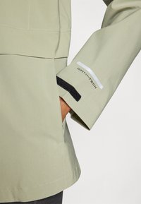 Svijetlozeleni vodootporni jakna s džepom i čičak zatvaranjem na manžetama. Uključuje Omni-Tech oznaku i elegantne detalje šivanja.