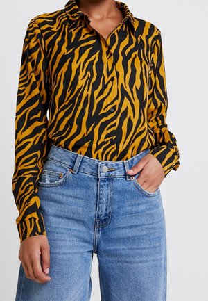 Camicia con bottoni in stampa zebra nera e oro, con maniche lunghe e colletto, abbinata a jeans blu a vita alta.
