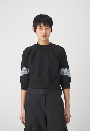 Sudadera negra con cuello redondo acanalado y mangas raglán. Presenta un detalle de encaje azul claro texturizado en las mangas. Tela suave, corte holgado.