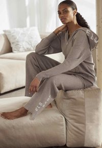 Hellgraues Loungewear-Set mit einem Reißverschluss-Hoodie und weiten Hosen. Mit Logo-Details auf dem Hoodie und dem Hosenbein. Weicher Stoff.