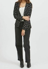 Schwarze Blazer mit weißem und lila Blumenmuster, kombiniert mit einem weißen Top, schwarzen Jeans und schwarzen Ankle-Boots. Glattes Material und figurbetonter Schnitt.