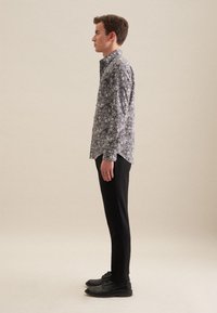 Koszula z długim rękawem w kwiatowy wzór w czerni i bieli, z zapięciem na guziki. W komplecie z czarnymi spodniami slim-fit i czarnymi butami.