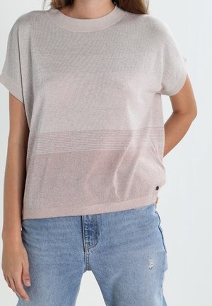 Kobieta w jasnoróżowej krótkiej dzianinowej bluzce z subtelnymi poziomymi paskami, zestawiona z jasnoniebieskimi jeansami.