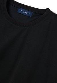 T-shirt in cotone nero con scollo rotondo e colletto a costine. L'etichetta riporta la scritta "PIOMBO" in bianco, su sfondo blu scuro. Texture liscia.