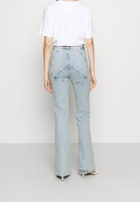 Světle modré zvonové džíny s vysokým pasem a jedinečnými trojúhelníkovými švy na zadní straně. Kombinováno s bílým tričkem s krátkým rukávem.