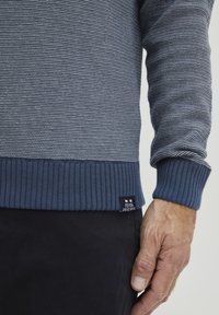 Sötétkék csíkos pulóver bordás mandzsettával és aljjal. Az alsó bal sarokban címke található. Az anyag lágy, texturált kötött.