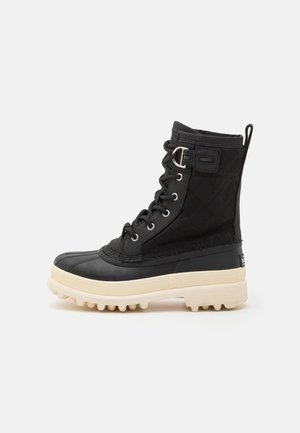 Zwarte waterdichte laars met een rubberen zool, bovenwerk van gequilt stof, vetersluiting en een contrasterende crème-kleurige platform.