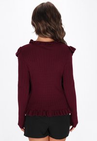 Burgundi csíkos pulóver fodros nyakkivágással és válldíszítéssel. Fennsíkos széle van és hosszú ujjak. Fekete sorttal párosítva.