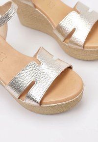 Sandalias de cuña de cuero plateado con parte superior texturizada, punta abierta, diseño de tiras anchas y plantilla envuelta en yute para mayor altura y comodidad.