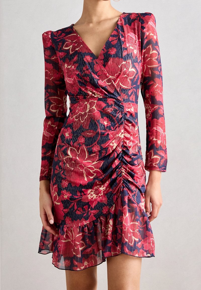 Robe mini à manches longues froncée avec imprimé floral rouge et rose sur fond bleu marine et un ourlet à volants.