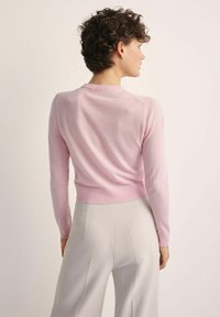 Różowy dopasowany sweter z długimi rękawami i okrągłym dekoltem, w zestawieniu z jasnoszarymi spodniami w wysokim kroju, podkreślającymi miękką fakturę.