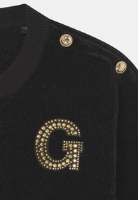 Schwarzer Velours-Pullover mit einem gerippten Kragen, goldfarbenen Metallknöpfen an der Schulter und einem goldnietenbesetzten 'G'-Logo auf der Vorderseite.