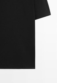 Sort t-shirt med korte ærmer, der viser kantene på sømmen og ærmerne mod en hvid baggrund, med ensartet glat stof uden synligt design.