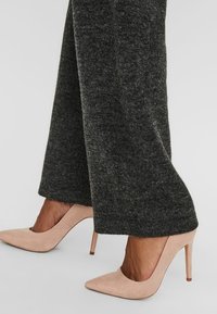 Zapatos de tacón beige con punta afilada, combinados con pantalones de pierna ancha de un gris oscuro, hechos de una tela suave y texturizada.