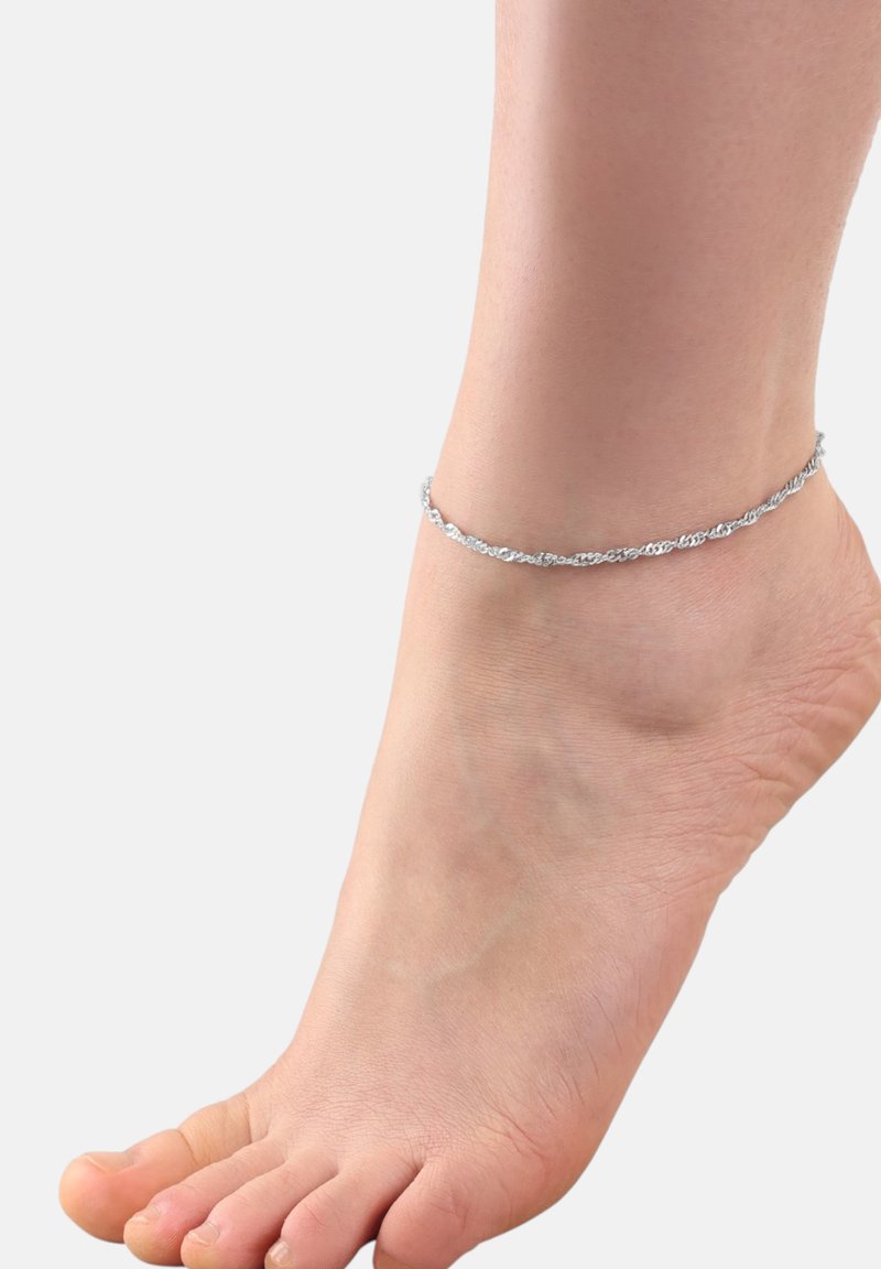 Tobillera de plata con delicados eslabones de cadena entrelazados, llevada en un pie descalzo, resaltando su diseño elegante y textura metálica.