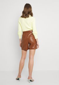 Bruna faux lädershorts med bältesmidja och två bakfickor, matchade med en ljusgul ribbad tröja.