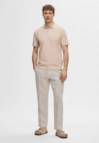 Polo beige, pantaloni in lino grigio chiaro e sandali aperti. Design semplice con una vestibilità classica e una texture morbida.