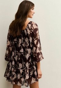 Vestido de chiffon floral con una base marrón oscuro y patrones beige claros, mangas tres cuartos y un dobladillo con volantes en capas.